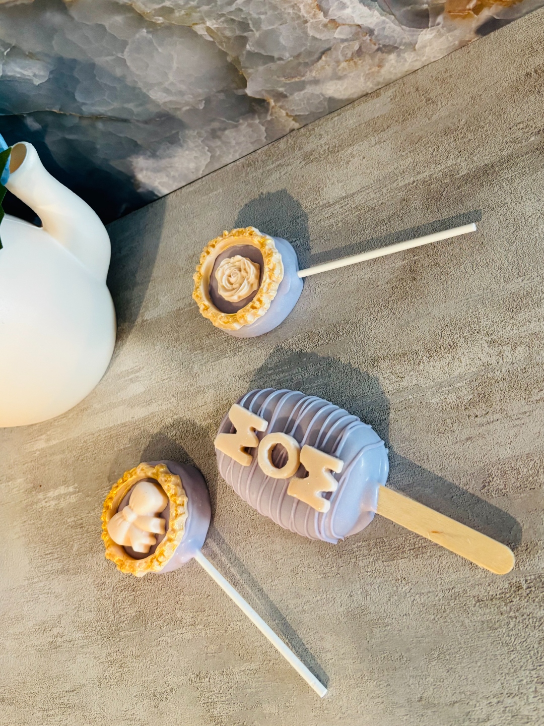Two custom lavender cakecicles with hand-piped rose and bow details, decorated by Sweet Sammye's